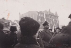 10. Zdjęcie z tłumu - wojsko na targowisku. W tle kamienice przy ul. św. Wawrzyńca, udekorowane licznymi flagami polskimi.