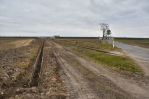 Pyszczyn, droga na Krzyszczewo. Obok toru w kierunku Nakła widać polną drogę w miejscu, gdzie miał być drugi tor. Po lewej odkopane w 2021 roku dawne koryto, które miało odwadniać torowisko. Zdjęcie 2021 rok